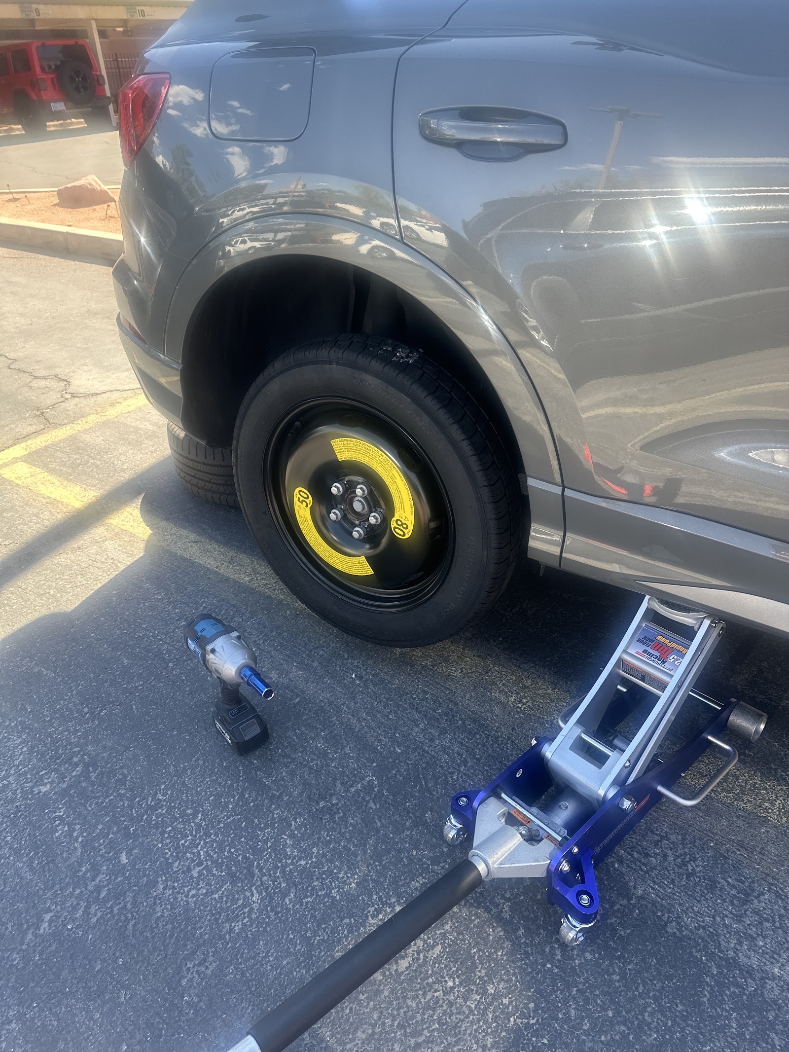 Spare tire installed on a gray SUV with a floor jack and impact wrench in use