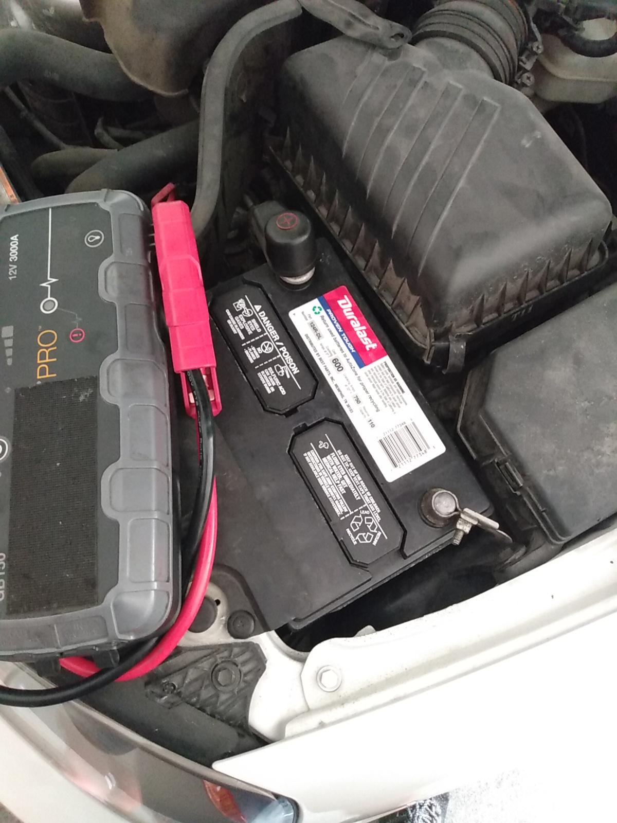 Portable jump starter connected to a Duralast car battery under the hood